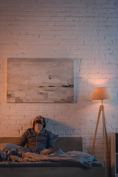 Tired man in pajama sitting with closed eyes on bed at night — Foto stock
