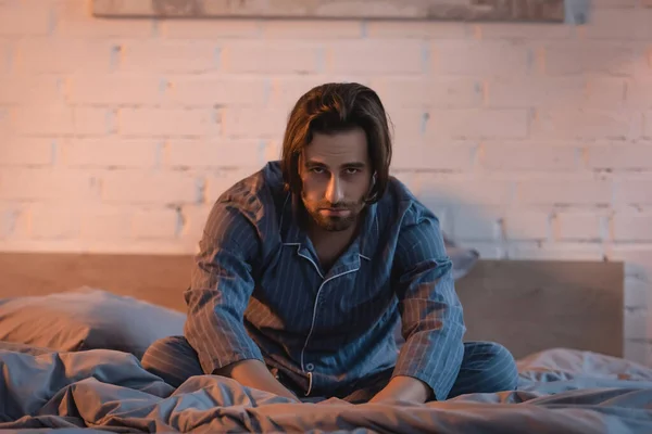 Upset man in pajama looking at camera while suffering from insomnia on bed — Stock Photo