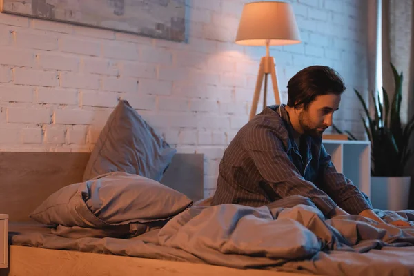 Bearded man sitting on bed while suffering from sleep disorder at night — Foto stock