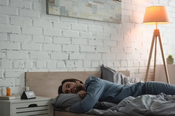 Junger Mann schaut auf Uhr, während er morgens unter Schlaflosigkeit im Bett leidet — Stockfoto