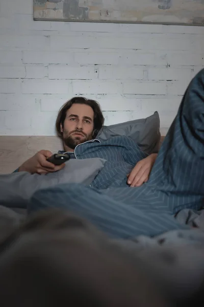 Bearded man in pajamas watching tv on bed at night — Stockfoto