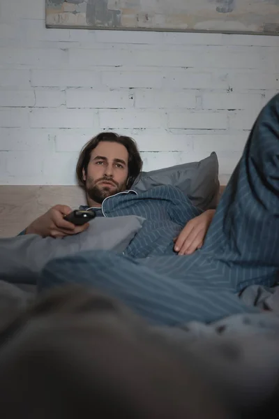 Bearded man in pajamas watching tv on bed at night — Stock Photo