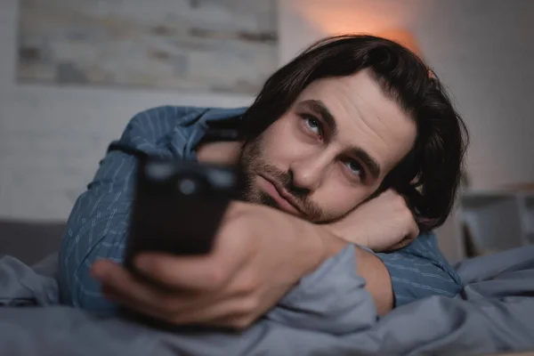 Sleepless man with remote controller watching tv in bedroom — Stock Photo