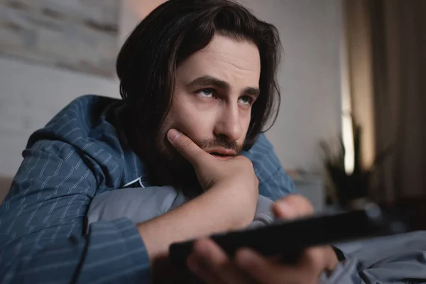 Young sleepless man with remote controller watching film on bed — Stockfoto