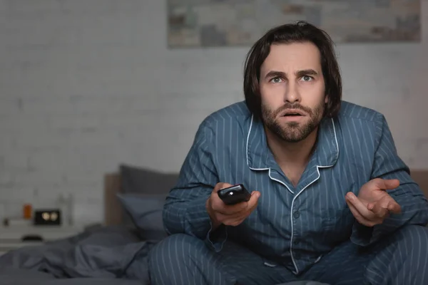 Confused man with insomnia holding remote controller on bed at night — Stock Photo