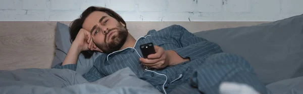 Erschöpfter Mann sieht fern, während er an Schlaflosigkeit im Bett leidet, Banner — Stockfoto