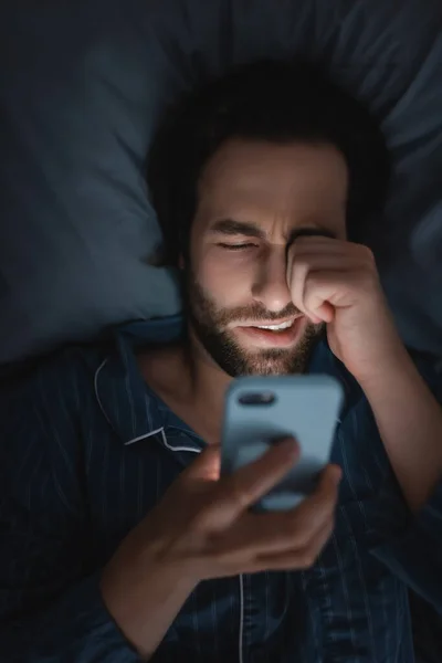 Top view of exhausted man in pajama using smartphone on bed at night — Fotografia de Stock