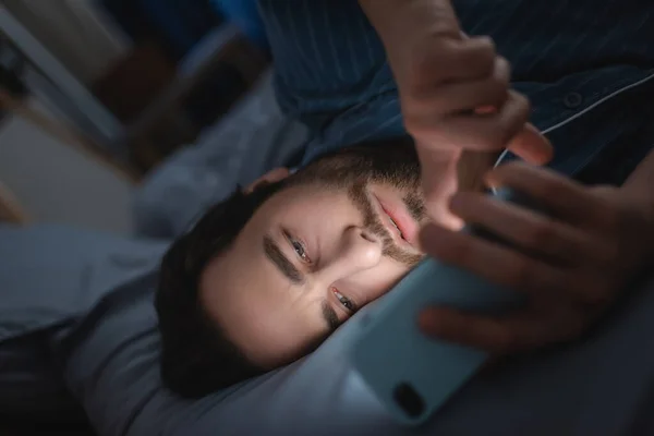 Bearded man with insomnia using mobile phone on bed — Stock Photo