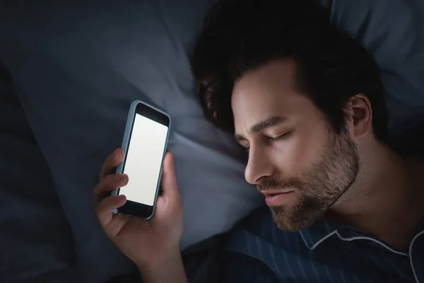 Top view of man in pajama holding smartphone with blank screen while sleeping on bed — Stock Photo