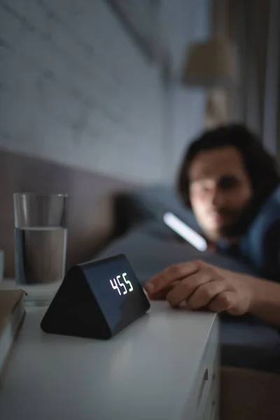 Blurred man touching alarm clock on bedside table at night — Stock Photo