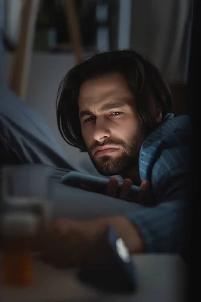 Dissatisfied man with insomnia holding smartphone on bed at home — Foto stock