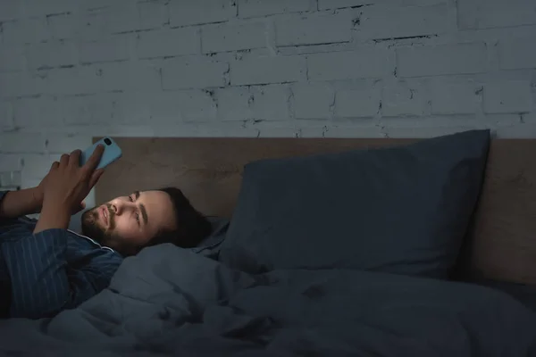 Молодой человек использует смартфон на кровати ночью — стоковое фото