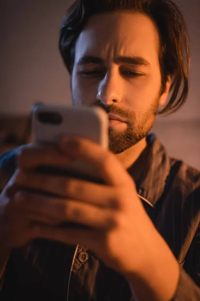 Бородатий чоловік у піжамі використовує смартфон у спальні — стокове фото