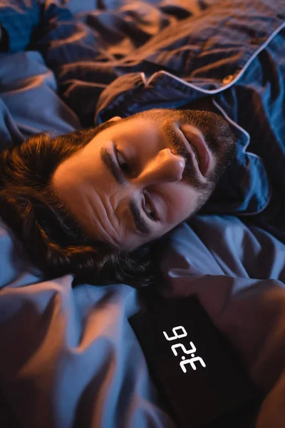 Worried man looking at alarm clock on bed at night — Stock Photo