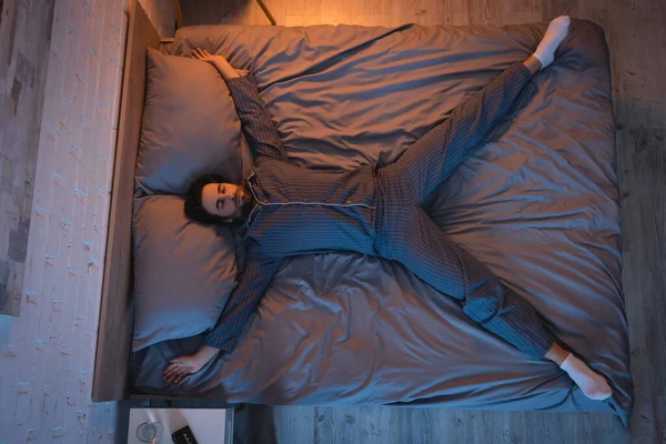 Vue du dessus de l'homme en chaussettes et pyjama dormant sur le lit à la maison — Photo de stock