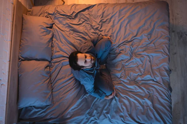 Вид сверху на человека с расстройством сна, сидящего с закрытыми глазами на кровати — стоковое фото