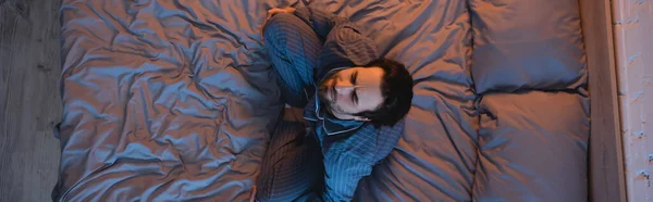 Vista aérea del hombre con los ojos cerrados sentados en la cama en casa, pancarta - foto de stock