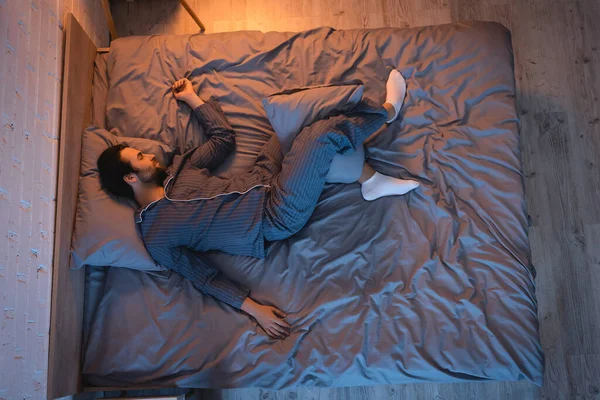 Vista lateral del hombre durmiendo en la cama en el dormitorio con iluminación en casa - foto de stock