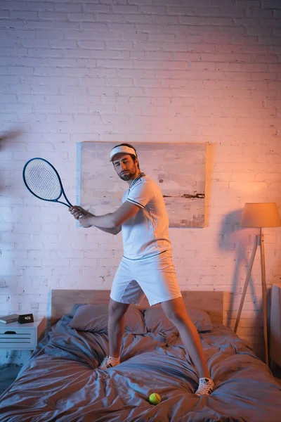 Sleepwalker in sportswear playing tennis on bed at night — Stock Photo