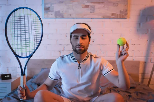 Sleepwalker with closed eyes holding tennis rocket and ball on bed — Stock Photo
