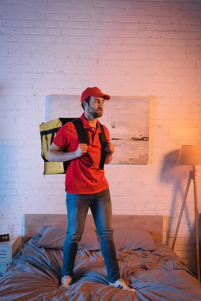 Sleepwalker in uniform holding thermo backpack on bed at night — Stock Photo