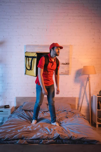 Deliveryman in uniform standing on bed while suffering from sleepwalking at night — Stock Photo