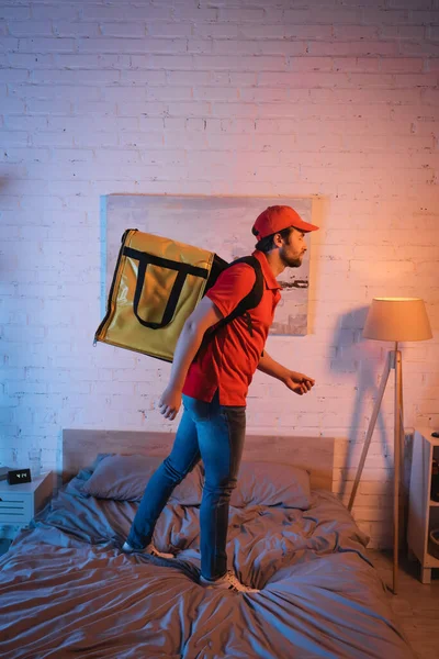 Side view of sleepwalker in uniform with thermo backpack standing on bed at night — Stock Photo