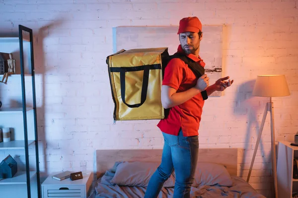 Запутавшийся лунатик в форме с терморюкзаком, стоящим на кровати — стоковое фото