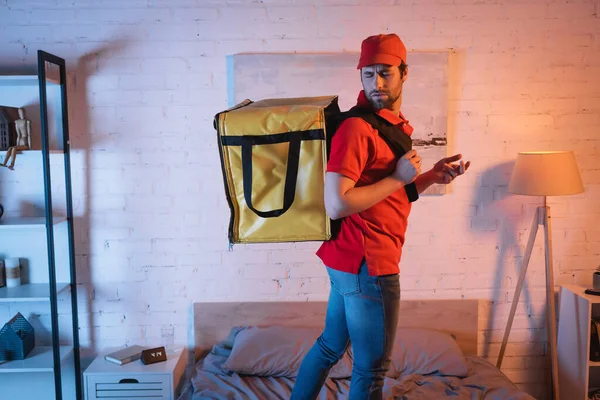 Confused sleepwalker in uniform with delivery thermo backpack standing on bed — Stock Photo