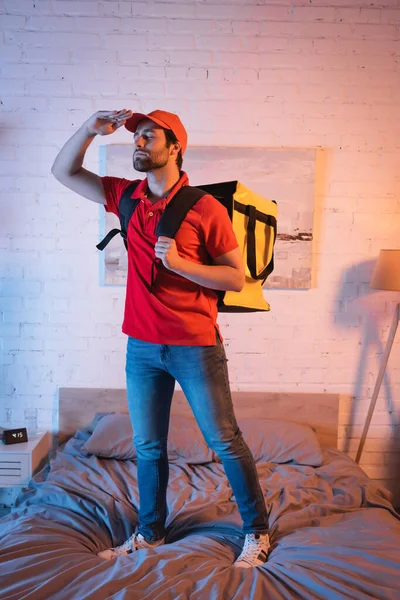 Young deliveryman with backpack gesturing while suffering from somnambulism on bed at home — Foto stock