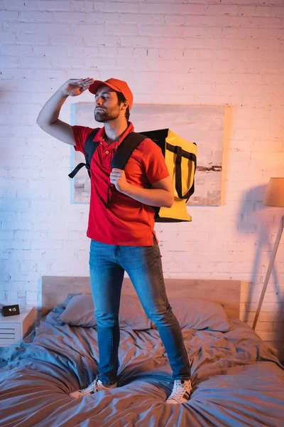 Young deliveryman with backpack gesturing while suffering from somnambulism on bed at home — Stockfoto