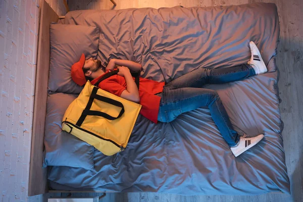 Side view of sleepwalker with delivery backpack sleeping on bed at night — Fotografia de Stock