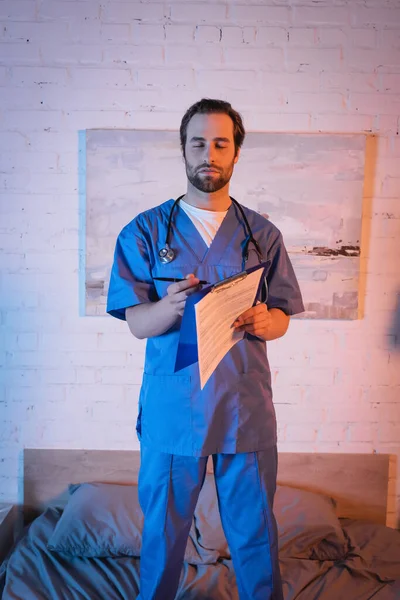 Somnambulist in doctor uniform holding pen and clipboard on bed at night — Stock Photo