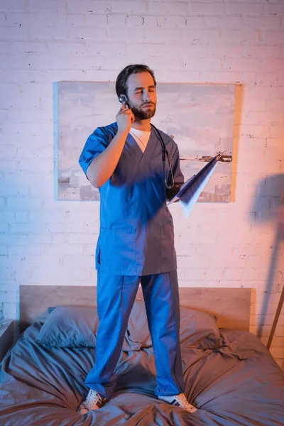 Sleepwalker in doctor uniform holding stethoscope and clipboard on bed — Stock Photo