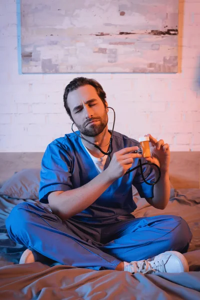 Somnambulist in doctor uniform holding stethoscope near pills on bed — Stock Photo