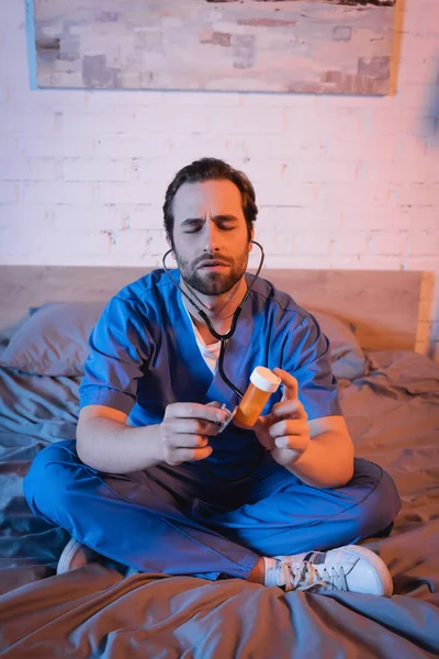 Sleepwalker in doctor uniform holding pills and stethoscope on bed at night — Stock Photo