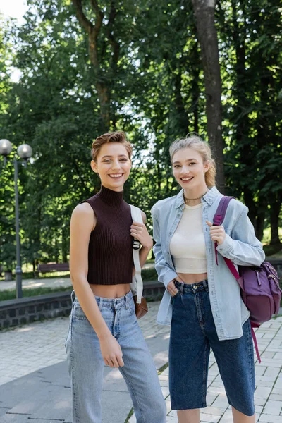 Cheerful students with backpacks looking at camera in park — Stock Photo