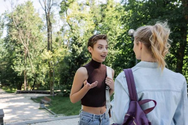 Joven estudiante con mochila hablando con un amigo en el parque - foto de stock