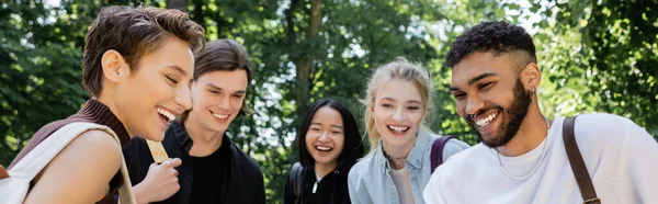 Estudiantes interracial positivos mirando hacia otro lado en el parque, pancarta - foto de stock