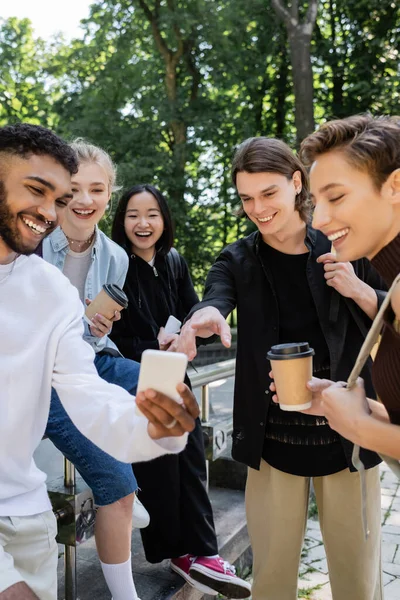 Multiethnic students with coffee to go looking at cellphone in park — Fotografia de Stock