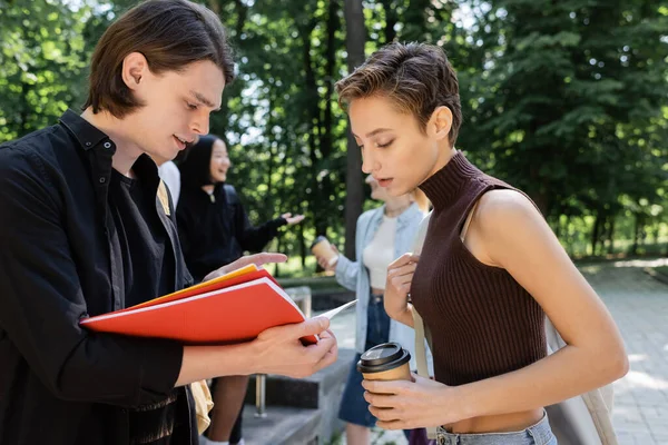 Students with coffee to go looking at notebook in park - foto de stock