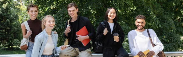 Allegro studenti interrazziale con zaini e quaderni guardando la fotocamera nel parco, banner — Foto stock