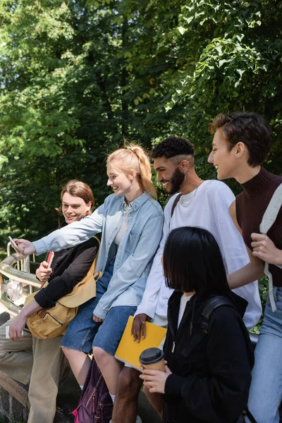 Smiling student taking selfie on smartphone with multiethnic friends in park — Stock Photo