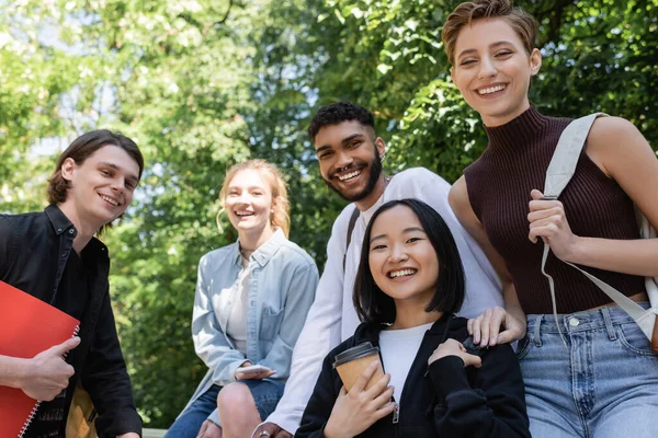 Allegri studenti multiculturali che guardano la fotocamera mentre trascorrono del tempo nel parco — Foto stock