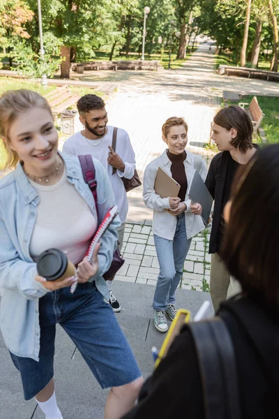 Cheerful multiethnic students with gadgets talking in park — Stock Photo