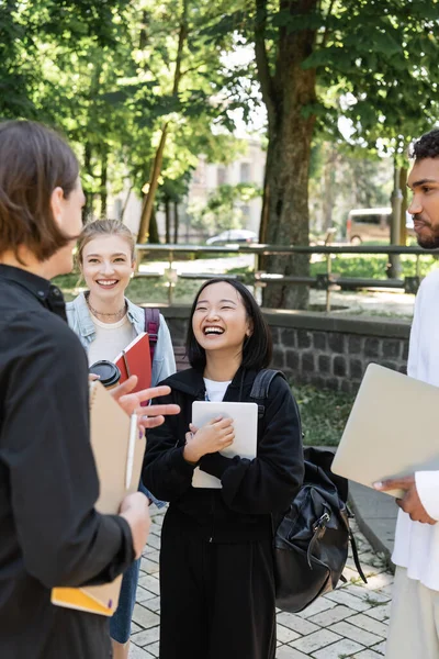 Joyeux asiatique étudiant tenant tablette numérique près d'amis multiethniques dans le parc — Photo de stock