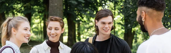 Estudiantes interraciales sonriendo y hablando en el parque de verano, pancarta - foto de stock