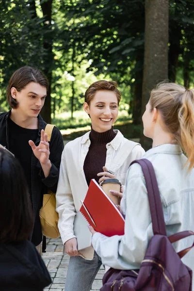 Позитивные студенты с блокнотами и кофе идут в парк — стоковое фото