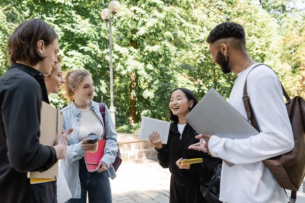 Азійські студенти тримають цифрову табличку біля усміхнених багатоетнічних друзів у літньому парку. — стокове фото