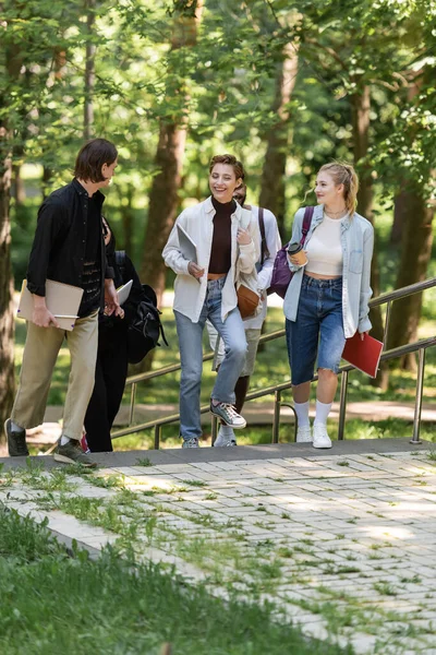 Alegres estudiantes multiétnicos hablando mientras caminan en el parque - foto de stock